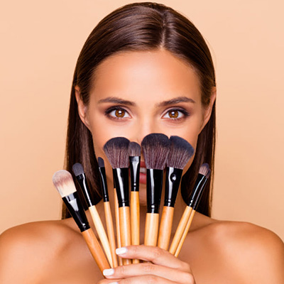 Woman covering half of her face with makeup brushes